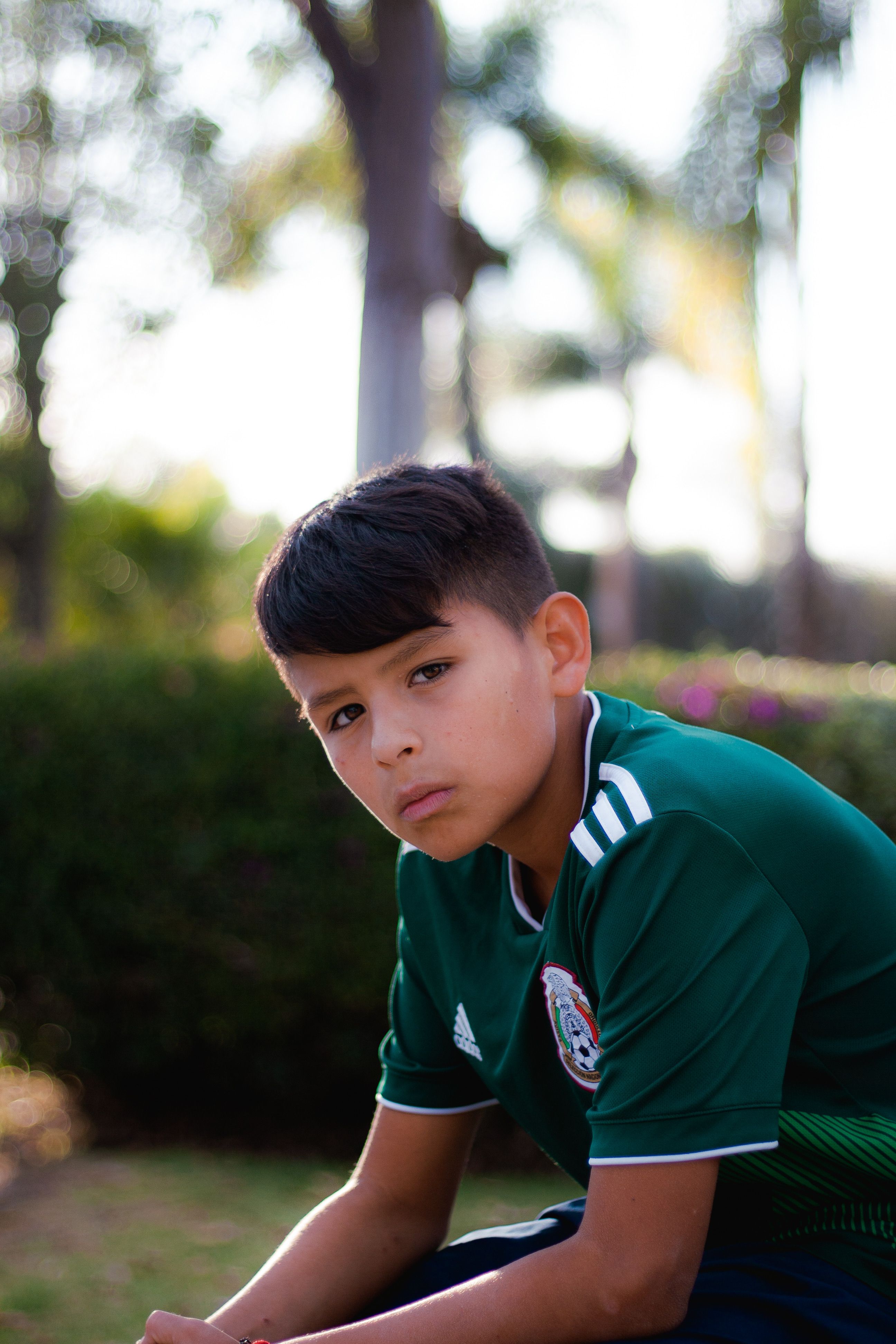 A young boy posing outdoors wearing a green soccer jersey, looking serious.
