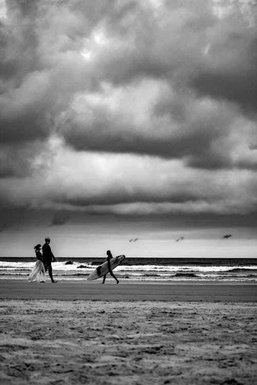 Grayscale Photo of People Walking on Beach under Cloudy Sky