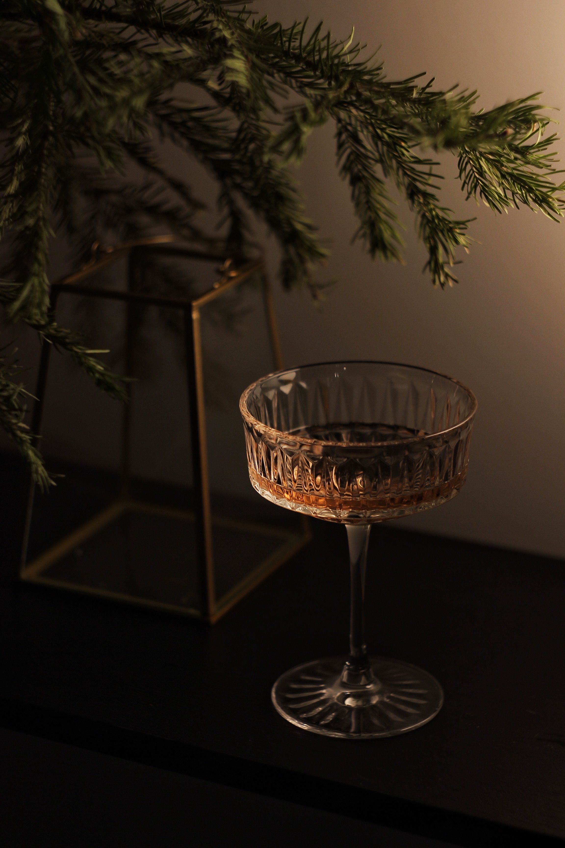 A festive glass of champagne with pine decor sets a warm holiday mood indoors.