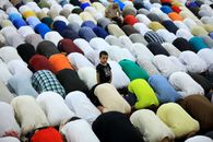 A group of people engaged in prayer inside a mosque, featuring diverse clothing patterns.