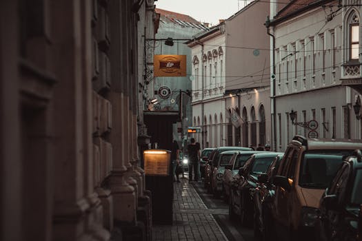 Explore the atmospheric narrow alley in Szeged's historic district, lined with parked cars and classic architecture.