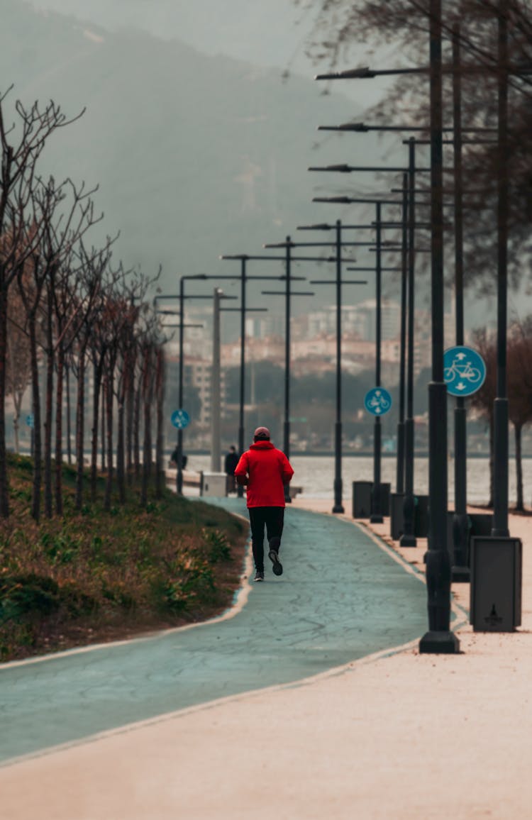 A Person In A Red Jacket Jogging At A Park