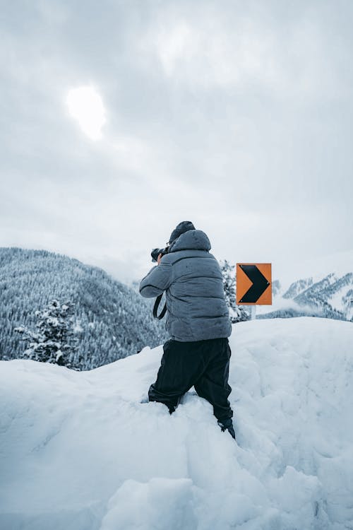 Free Person in Gray Jacket and Black Pants Standing on Snow Covered Ground Stock Photo