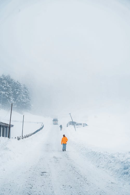 A Person in Yellow Jacket Walking on Snow Covered Road