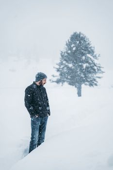 A man in a beanie and jacket standing in a snowy, serene winter landscape.