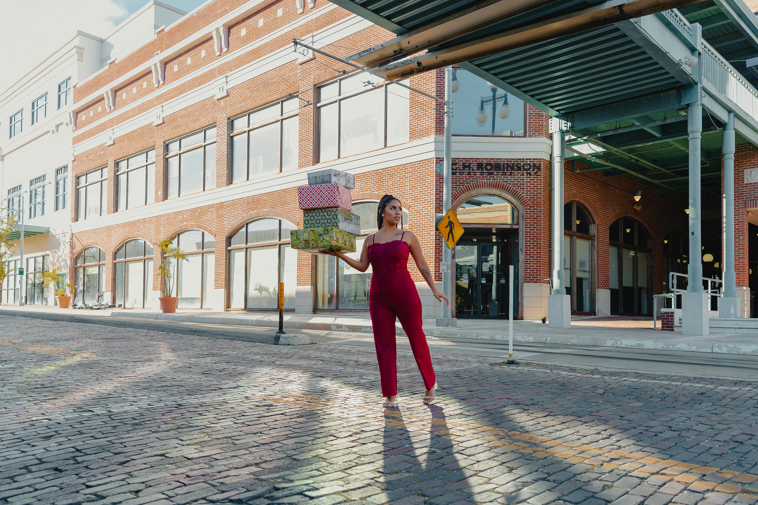 Stylish woman in red carrying gift boxes across an urban street in Tampa, FL.