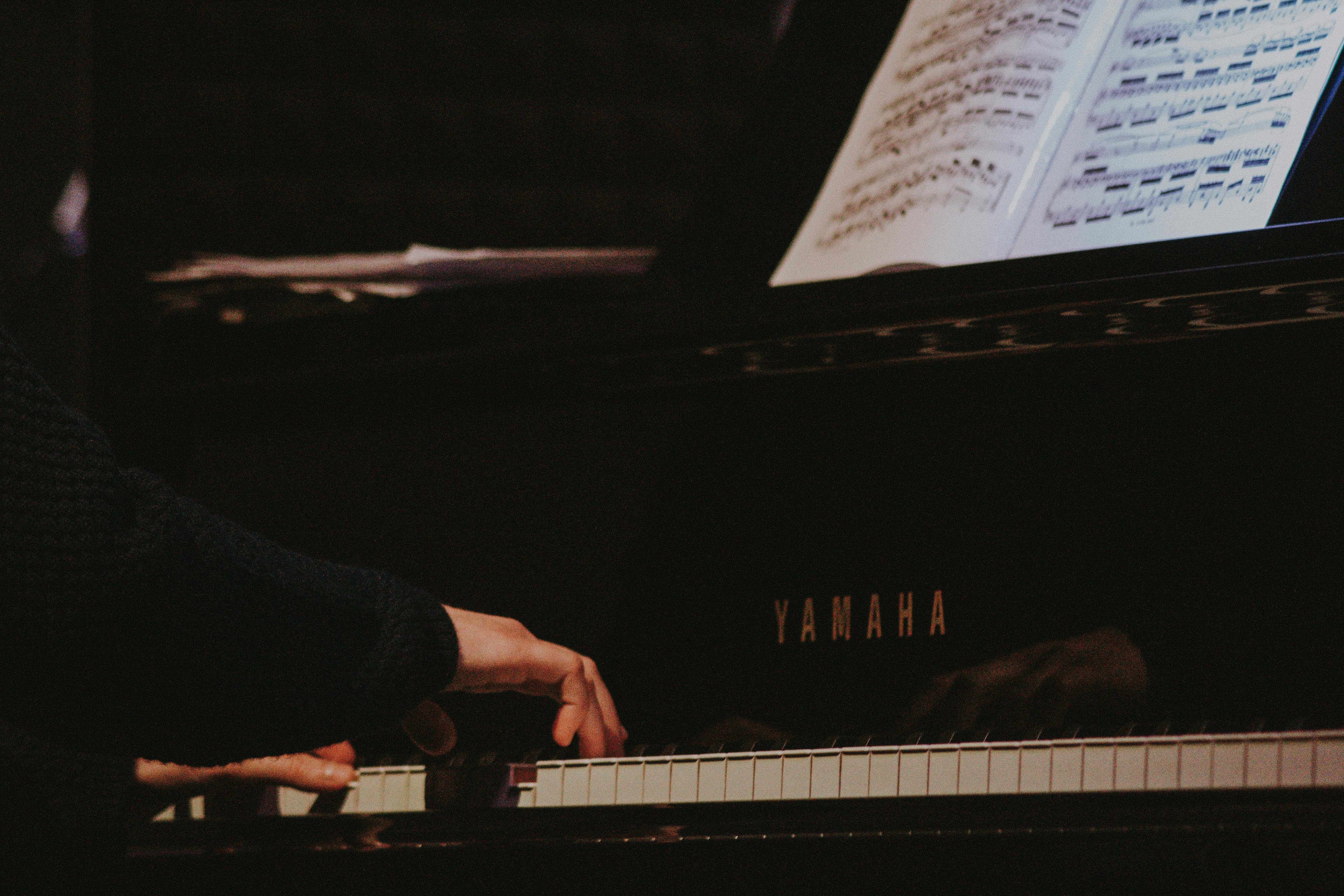 Close-up of hands playing a Yamaha grand piano with sheet music displayed.