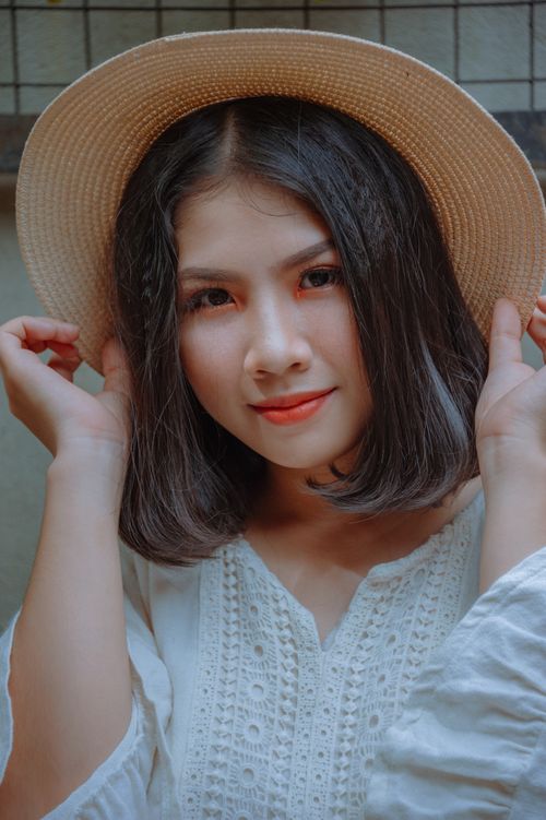 Free Enchanting portrait of a young woman in a white dress and straw hat indoors. Stock Photo