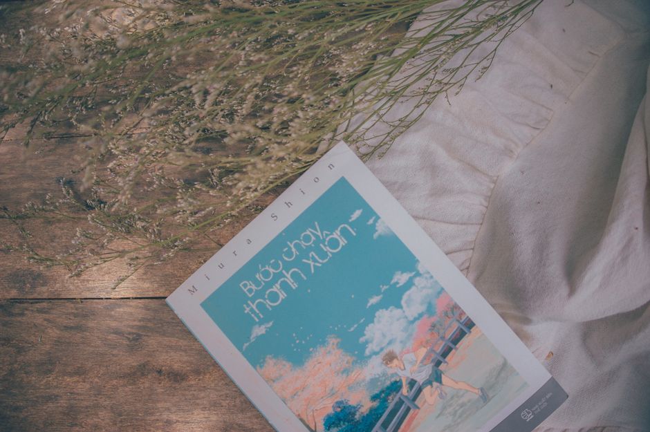 Artistic flat lay of a book with dried flowers on a wooden surface.