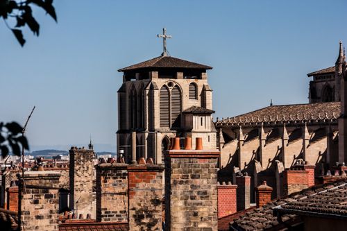 Free View of a historic church facade in Lyon, featuring a cross and traditional rooftops against a blue sky. Stock Photo