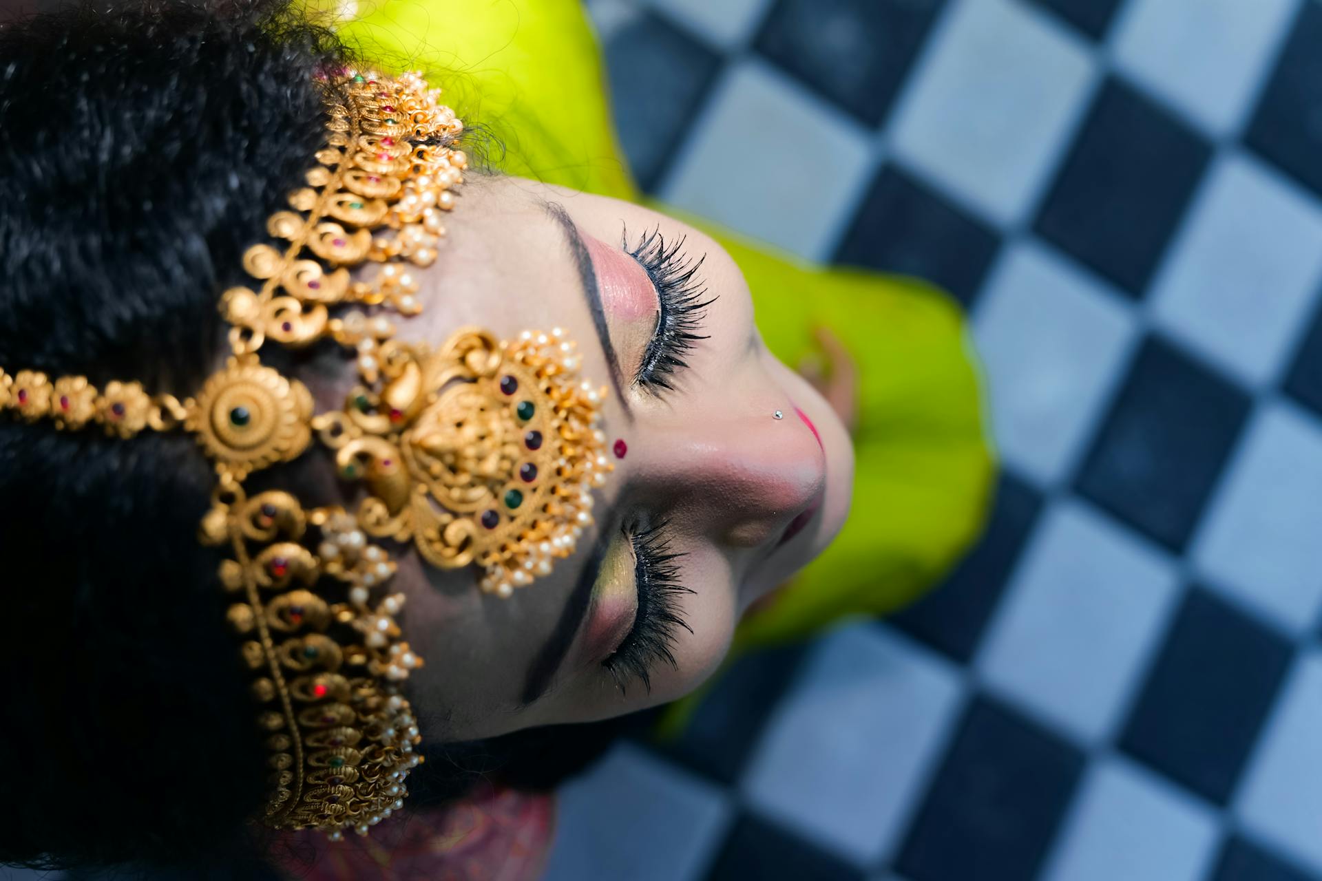 Top view of an Indian woman adorned in gold jewelry and traditional attire, beautifully captured indoors.