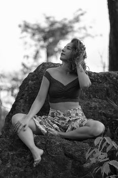 Grayscale portrait of a woman sitting barefoot on a rock, exuding tranquility and natural beauty.