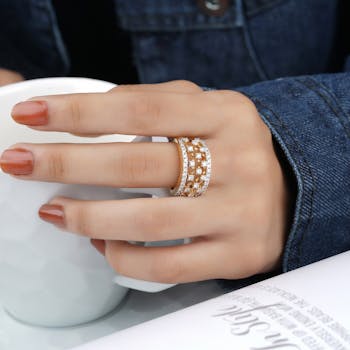 Close-up of a hand with a diamond ring holding a ceramic cup. Denim jacket visible.