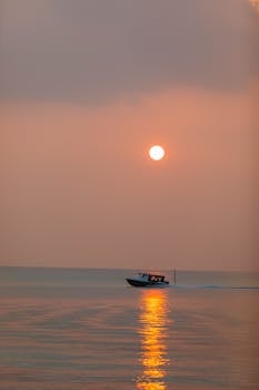 A boat gliding on the tranquil ocean during a vibrant sunset, casting a warm reflection.