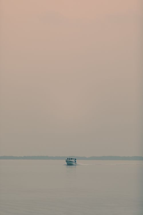 Free A boat quietly cruises on calm waters under a pastel sky, capturing tranquility and peace. Stock Photo