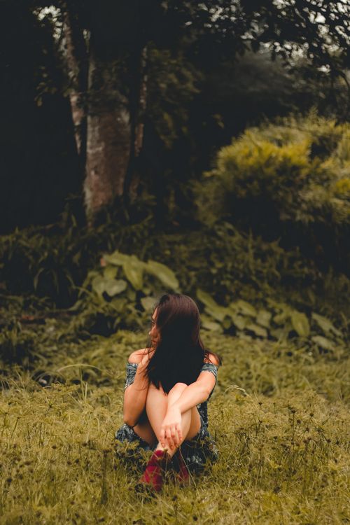 Free Woman sitting in a lush forest, embracing peace and solitude on a sunny day. Stock Photo