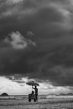 Black and white beach scene with a vendor cart and dramatic cloudy sky in São Paulo, Brazil.