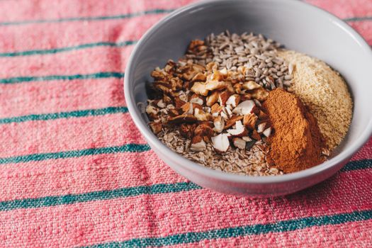 A mix of seeds, nuts, and spices in a bowl on a pink textured cloth, showcasing healthy food.