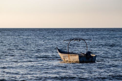 Free An old fishing boat floats quietly on the serene sea at sunset, showcasing calm beauty. Stock Photo