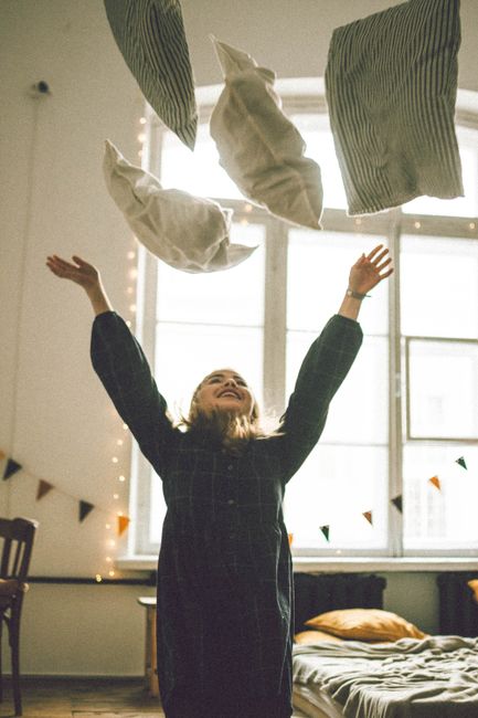 A young girl joyfully throws pillows in a bright, cozy bedroom.