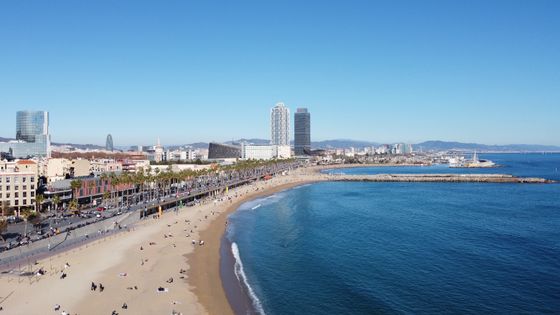لقطة جوية مذهلة لشاطئ برشلونة وأفق المدينة في يوم صافٍ، تلتقط الساحل النابض بالحياة.