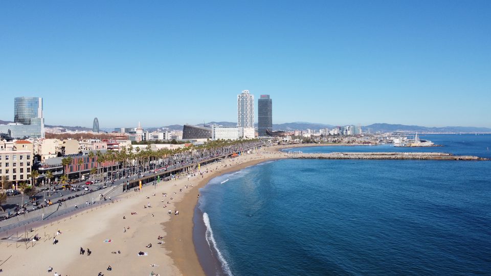 لقطة جوية مذهلة لشاطئ برشلونة وأفق المدينة في يوم صافٍ، تلتقط الساحل النابض بالحياة.