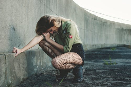 Woman Squatting Near Gray Concrete Wall at Daytime