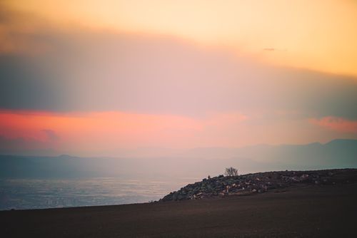 Free A tranquil landscape showcasing a vibrant orange sunset over distant hills, evoking a sense of peaceful solitude. Stock Photo