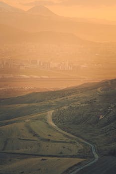 Explore a serene hilly landscape at dawn with gentle fog and distant mountains.