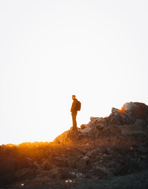 Free A lone hiker stands on a rocky mountain ridge during a dramatic golden sunset, capturing a sense of adventure. Stock Photo