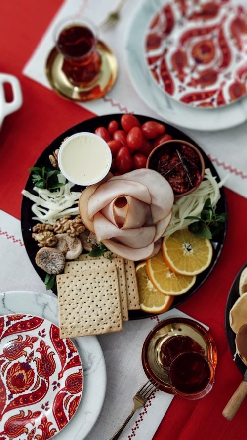 Free Elegant charcuterie board featuring ham, crackers, fruits, and nuts with decorative red pattern plates. Stock Photo