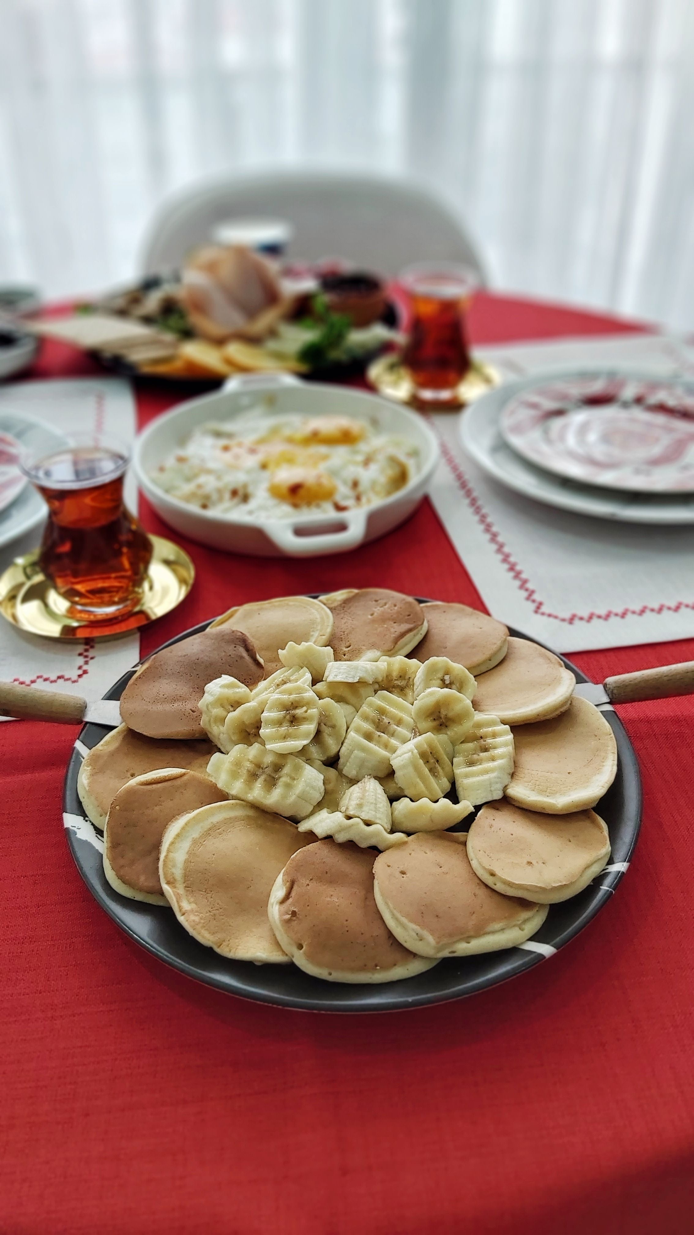 A cozy breakfast setup featuring pancakes and black tea on a red tablecloth.