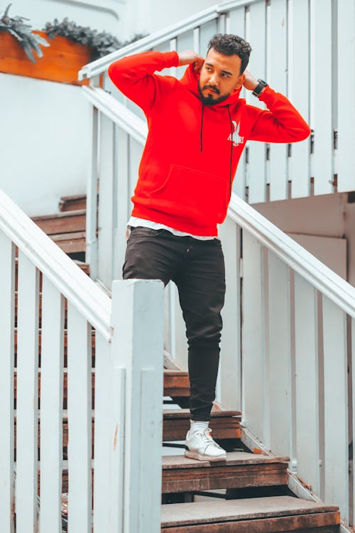 Free Man in Red Hoodie and Black Pants Standing on Wooden Staircase Stock Photo