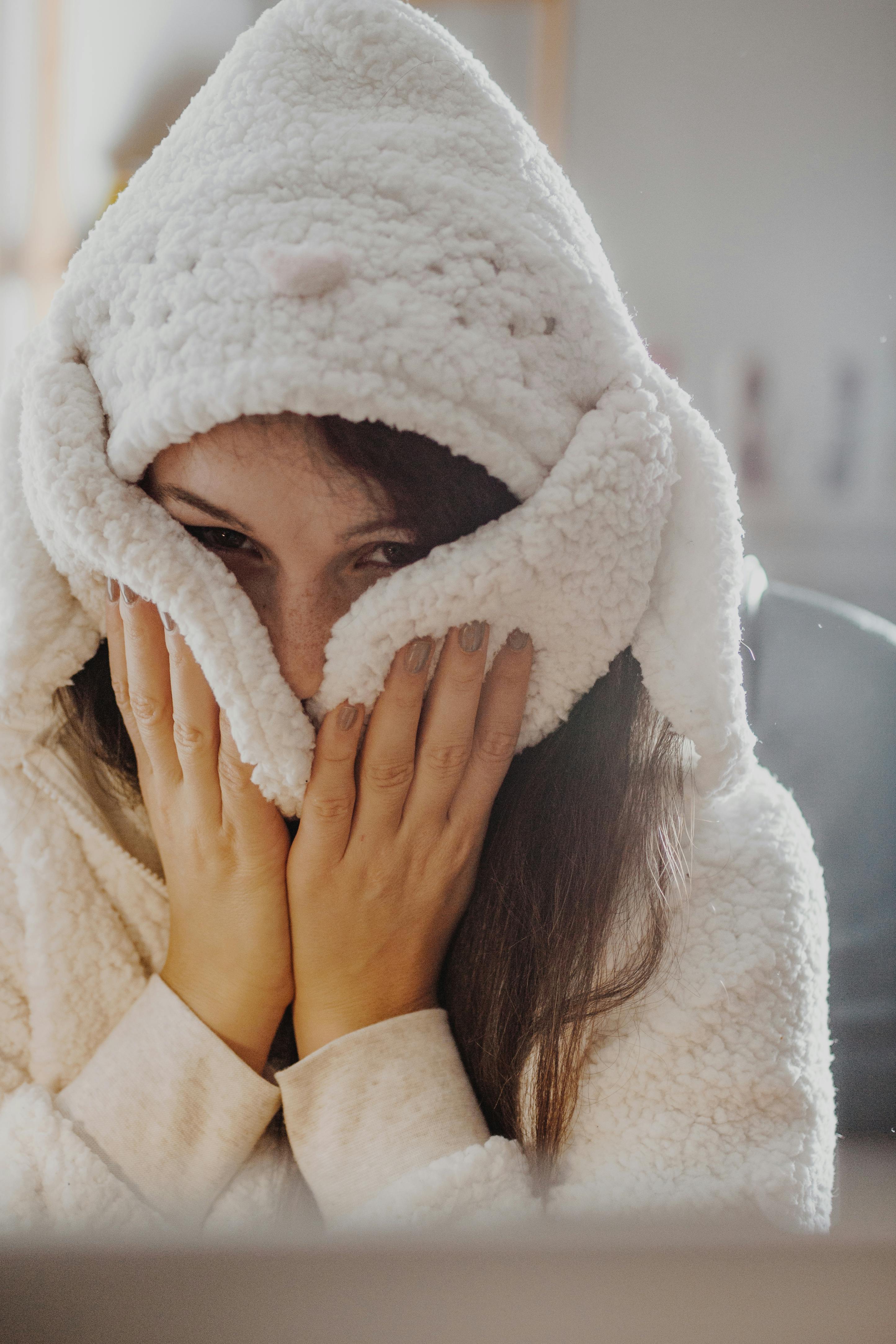 A woman warmly dressed in a teddy bear hoodie enjoying comfort indoors. Perfect for lifestyle themes.