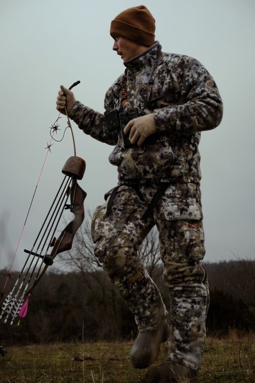 Free A man in camouflage gear holding a bow, preparing for a hunt outdoors. Stock Photo