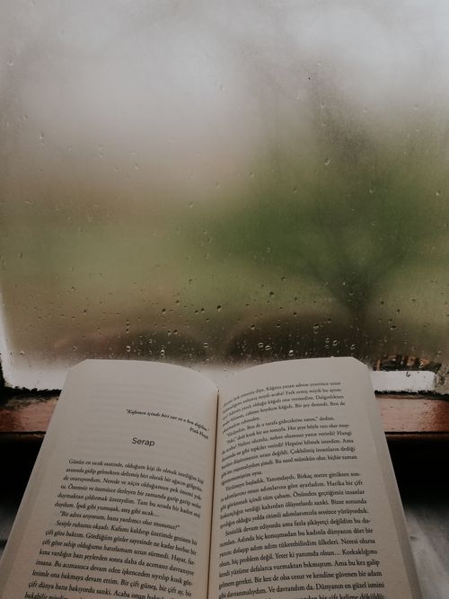 Free An open book by a rain-streaked window, perfect for a cozy reading atmosphere. Stock Photo