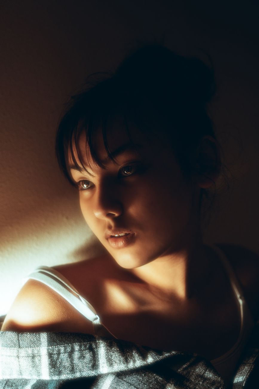 Artistic portrait of a young woman in warm, shadowy lighting with a thoughtful expression.