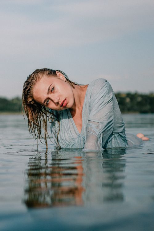Free Elegant woman in blue attire poses gracefully half-submerged in water under clear sky. Stock Photo