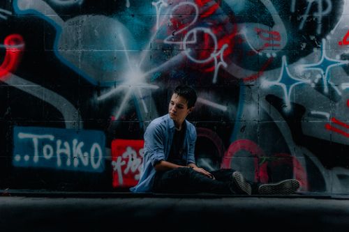 Free A young man sits pensively against a vibrant graffiti wall, evoking an urban vibe. Stock Photo