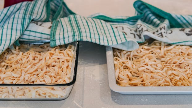 Fresh homemade pasta drying on trays, covered with kitchen towels, ready for cooking.