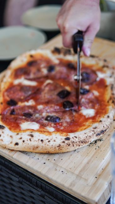 Photo by Anna Guerrero on Pexels Close-up of a hand slicing a delicious Italian pizza with olives on a wooden board.