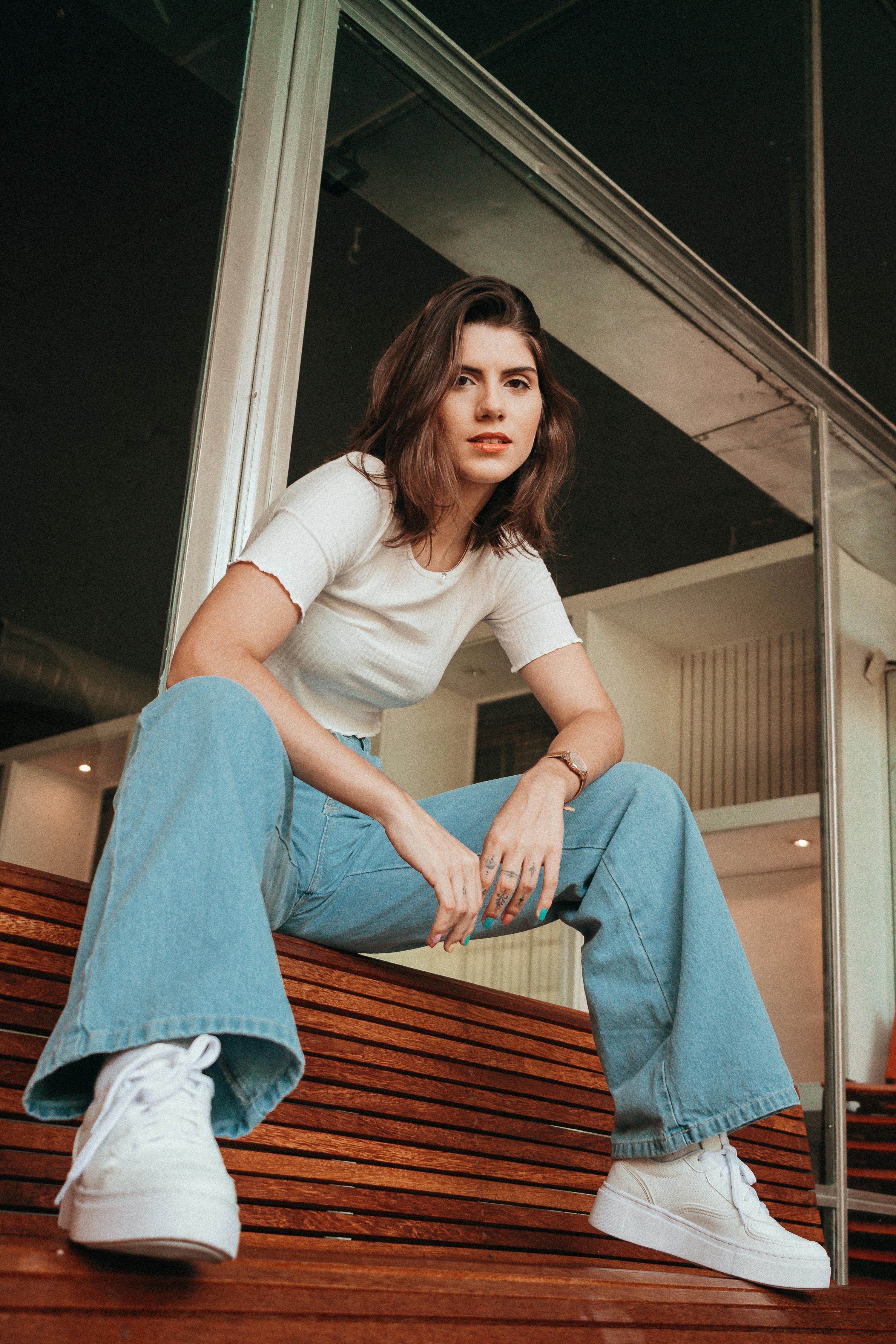 Confident woman in casual attire sitting on a wooden bench outdoors, showcasing style and poise.