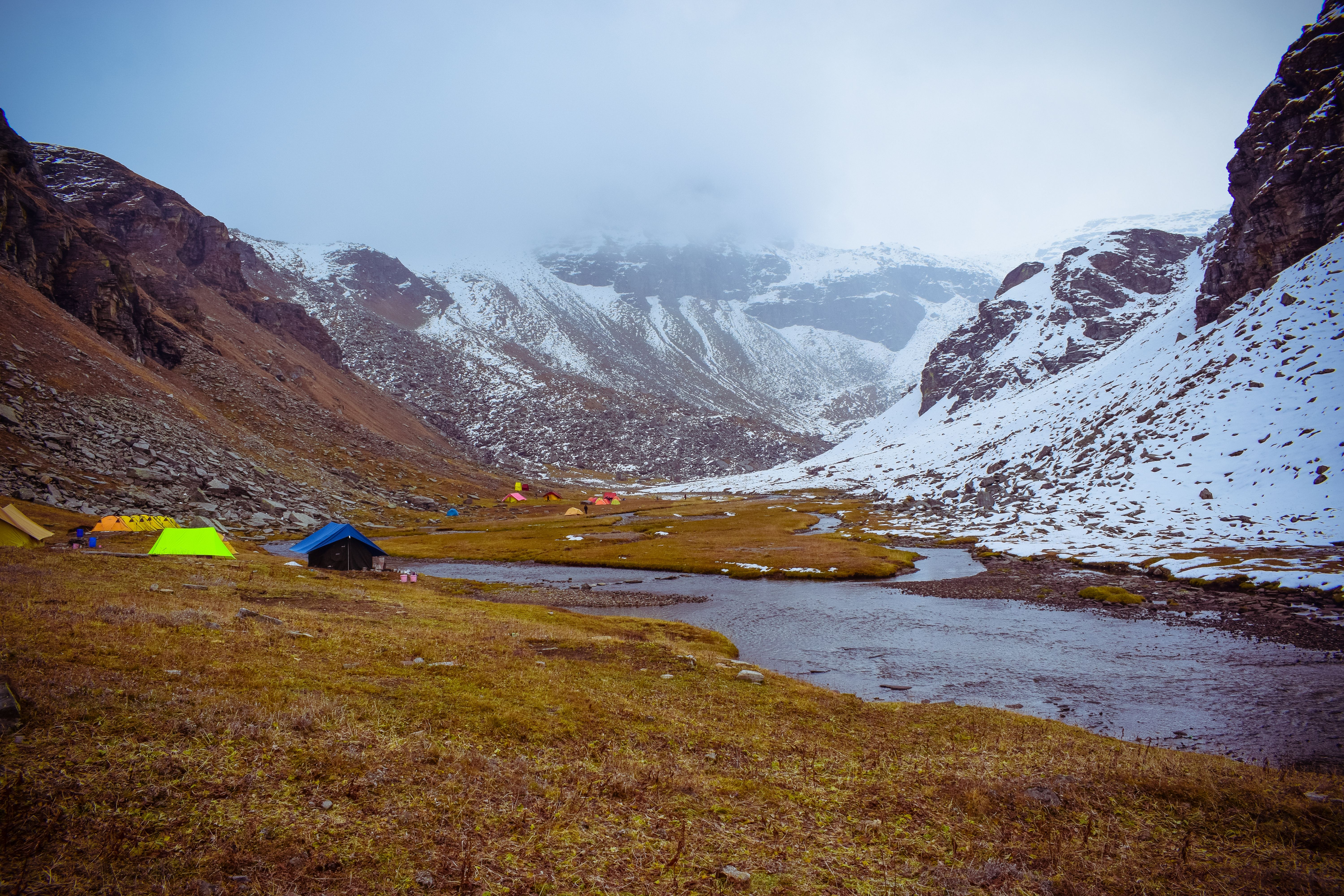 Stunning valley landscape in Himachal Pradesh with colorful tents and snow-capped mountains.