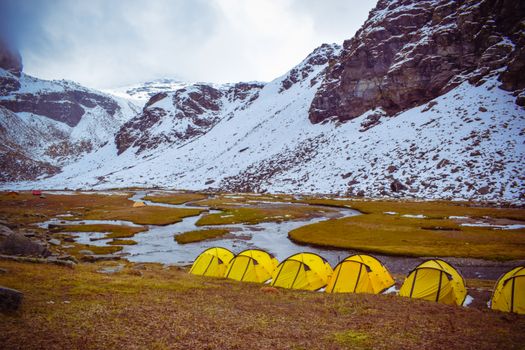 Yellow tents in snowy mountains of Himachal Pradesh, India, camping by the stream.