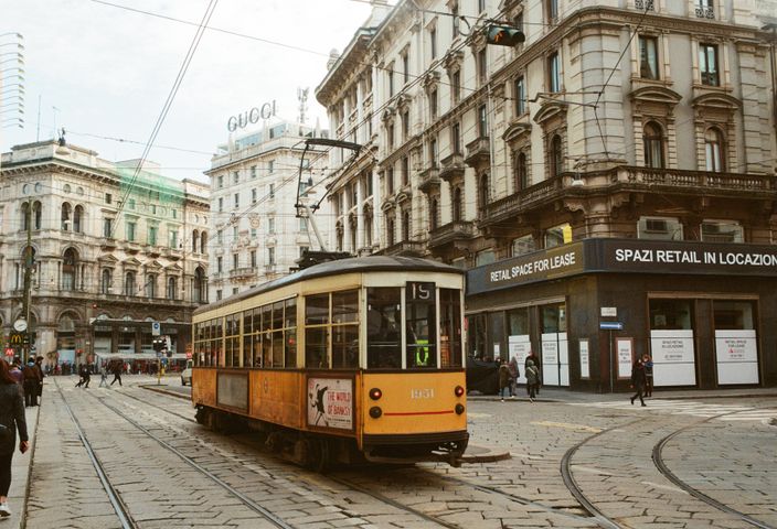 A vintage tram navigates the bustling streets of Milan, Italy, showcasing classic architecture.