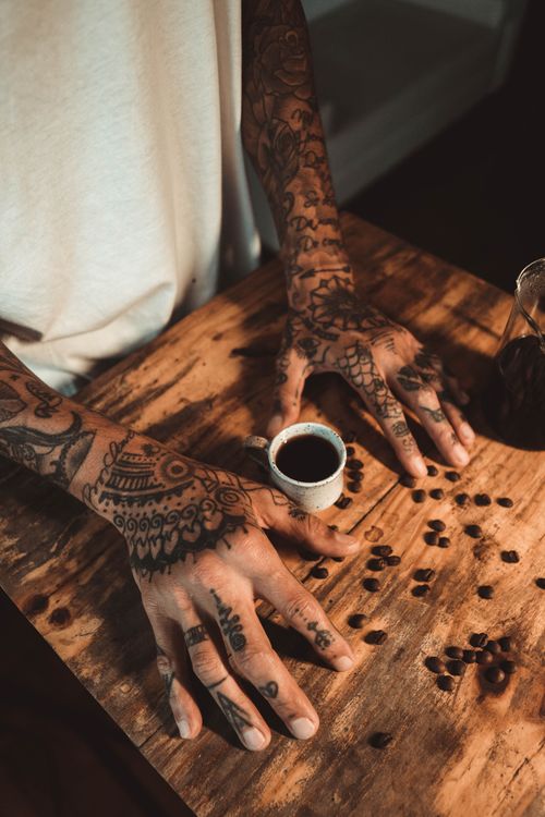 Free Artistic shot of tattooed hands holding espresso on a rustic table, São Paulo. Stock Photo