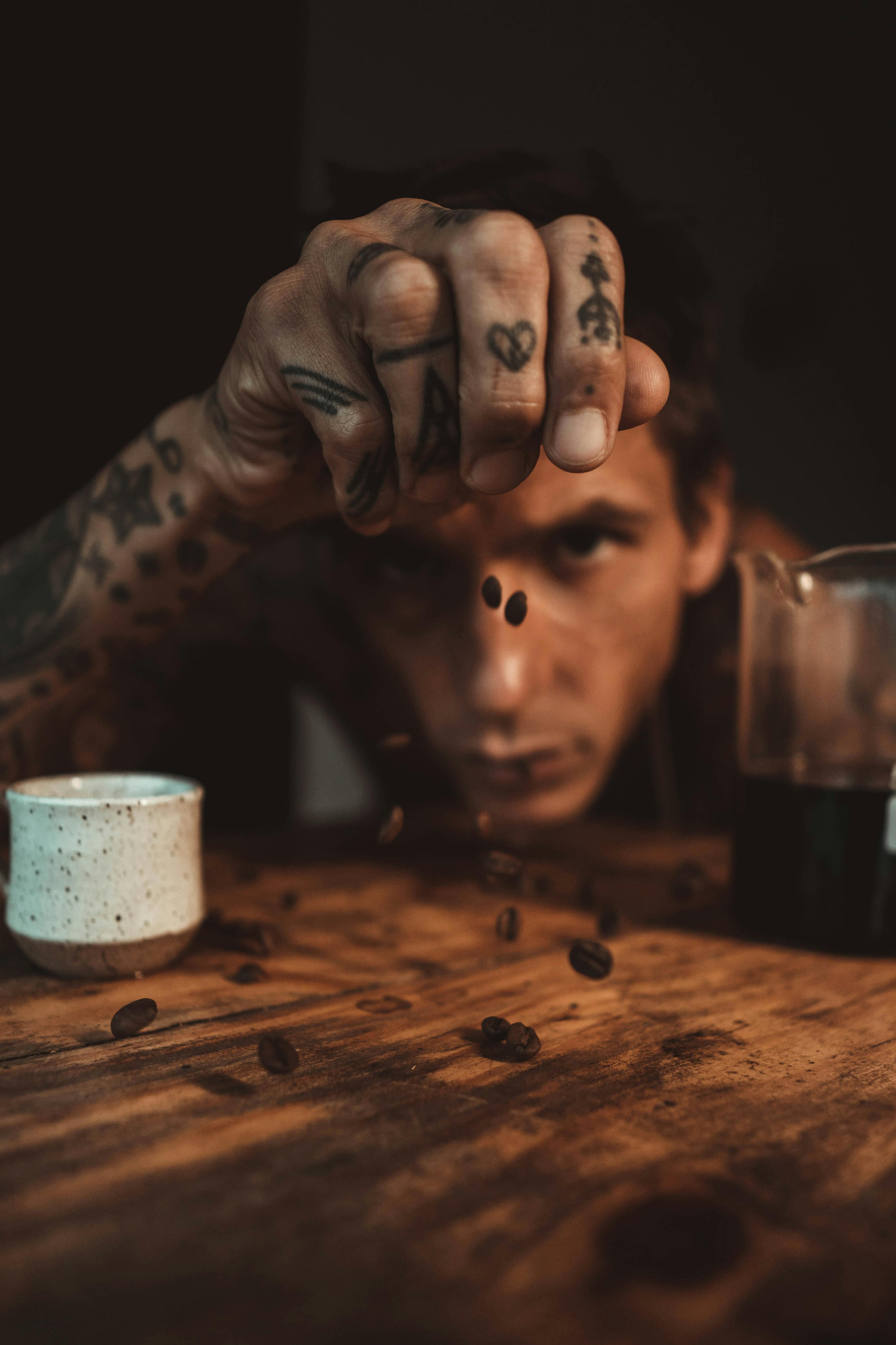 Free Close-up of a tattooed barista levitating coffee beans over a wooden table, creating a dynamic scene. Stock Photo