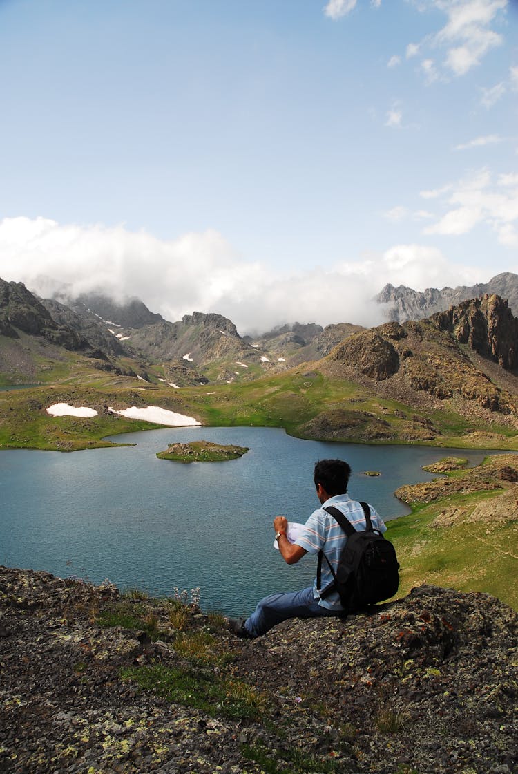 Back Of A Man Sitting On The Rocks Above A Lake