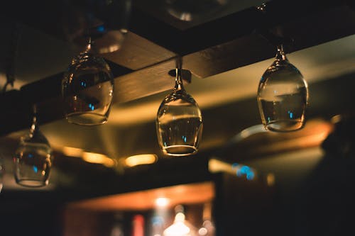 Selective Focus Photography of Wine Glass Hanging on Black Wooden Rack