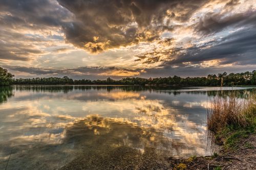 Free A breathtaking sunset over a serene lake with dramatic cloud reflections creating a picturesque landscape. Stock Photo